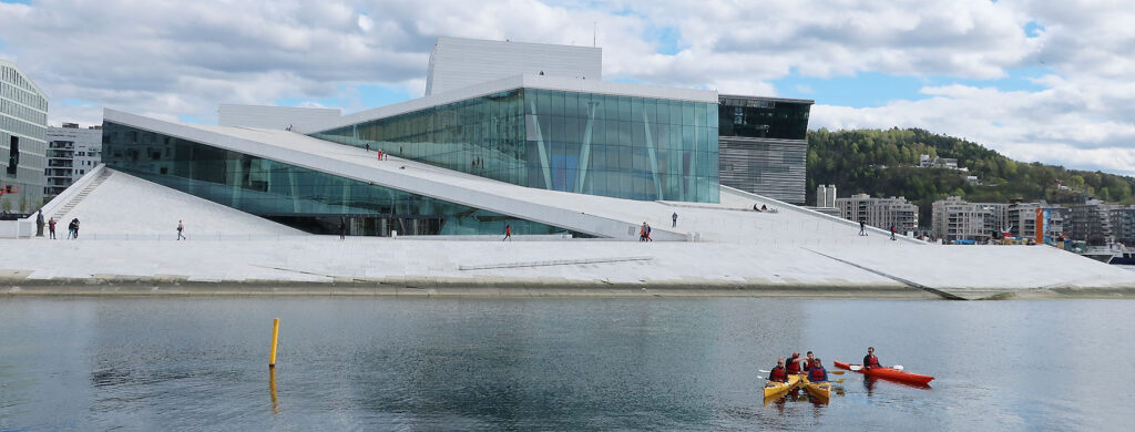 En gruppe padlere ligger i vannet i forgrunnen. Oslo operahus i bakgrunnen.