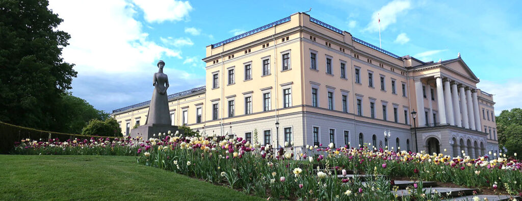 En statue av Dronning Maud blant tulipaner. I bakgrunnen ruver slottet. 